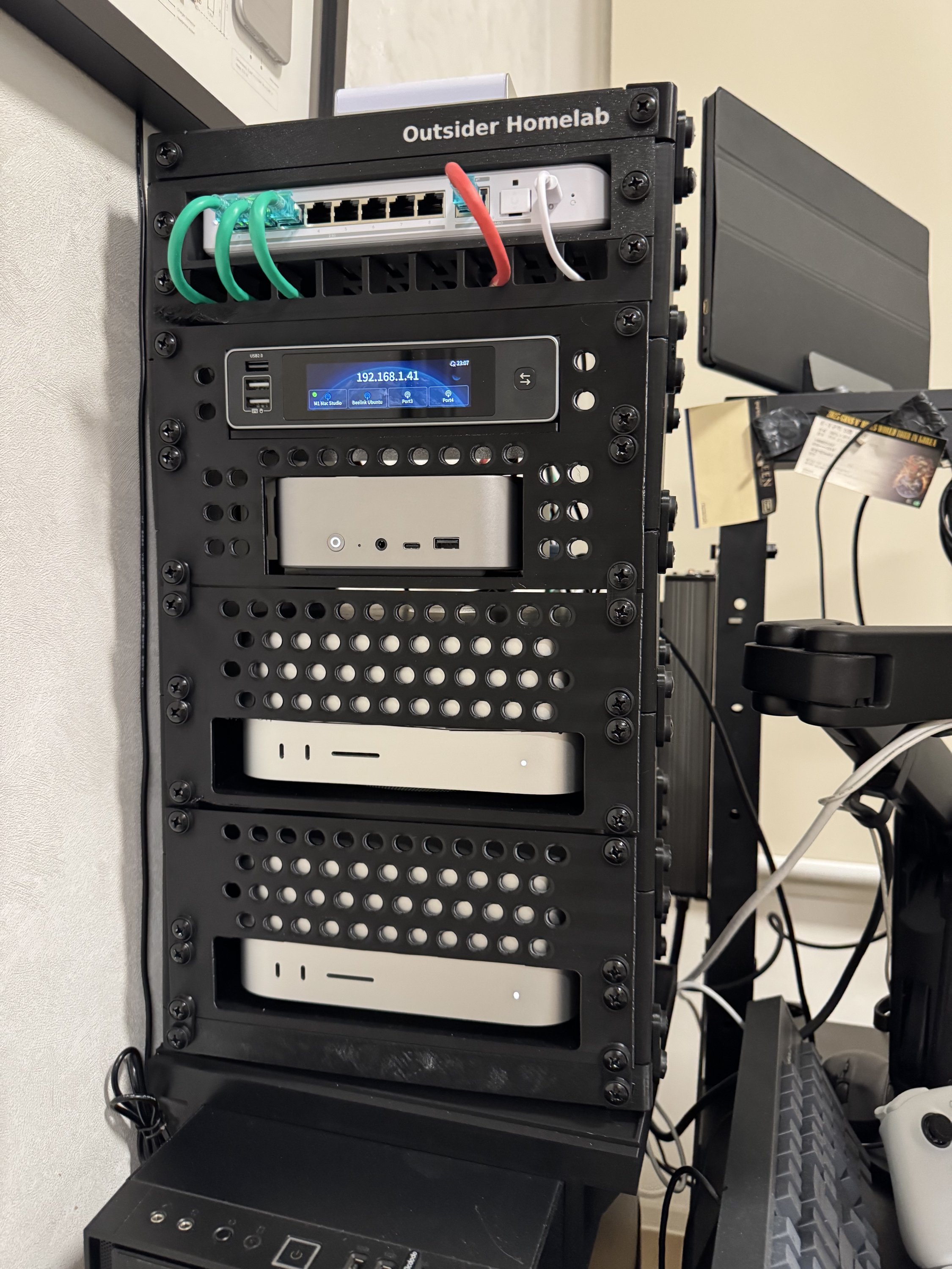 Outsider Homelab 라벨이 붙은 검은색 미니 랙에 위에서부터 네트워크 스위치, IP 주소를 띄운 터치 디스플레이, 미니 PC, Mac Studio 두 대가 장착되어 있다.